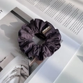 Détail d'un chouchou plissé en tissu violet foncé avec étiquette de marque tissée - Violet