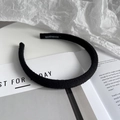 Dettaglio di un cerchietto nero in maglia con etichetta fatta a mano su sfondo minimal - Nero