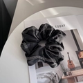 Detail eines schwarzen Satin-Haargummis mit glitzernden Strasssteinen am Rand auf Buch - Schwarz