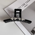 Dettaglio ravvicinato di una pinza per capelli nera con perle finte e decoro floreale - Bianco