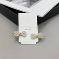 Dettaglio di eleganti fermagli a fiocco dorati con perle bianche su cartoncino - Perla d'oro con zircone
