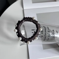 Dettaglio dell'elastico per capelli marrone scuro con perle bianche su sfondo minimalista - Marrone