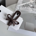 Detail of coffee brown bow hair clip with satin texture on display card - Khaki