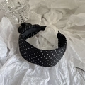 Dettaglio di un cerchietto nero vintage a pois bianchi su uno sfondo bianco strutturato - Stile a Pois