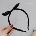 Gros plan d'un serre-tête noir en satin avec oreilles de lapin, tenu à la main sur fond gris - Noir