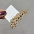 Dettaglio di un fermaglio per capelli a piuma dorata con perle su scheda espositiva - Perla Oro