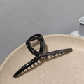 Dettaglio di una grande pinza per capelli in metallo nero lucido su un vassoio ceramico - Canna di Fucile