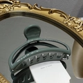 Primer plano de una pinza para el pelo verde grisáceo sobre un espejo dorado vintage - Verde Frijol