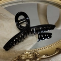 Close-up of minimalist glossy black crossover hair claw clip on vintage gold mirror - Black