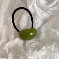 Detail shot of a glossy olive green bean-shaped charm on a black elastic hair tie - Mustard Green