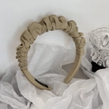 Close-up of pleated beige satin headband with a handmade label on a textured background - Greenish Beige