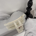 Dettaglio di una grande molletta per capelli crema con perle e fibbia dorata su uno specchio - Beige