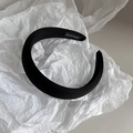 Detail of a padded black satin headband featuring a handmade woven label on a white background - Black