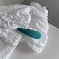 Gros plan d'une barrette à cheveux en tissu bleu cyan sur un fond de papier minimaliste - Vert paon