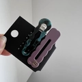 Detalle de pinzas onduladas de acetato con textura de mármol y logo dorado en tarjeta - Juego de Textura Azul Negro y Morado Mate / Rosa Púrpura