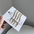 Detail of four golden wavy minimalist hair clips on white card packaging - Gold