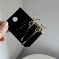 Pair of gold metal bow hair clips on black display card held by hand showing the design - Gold
