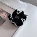 Dettaglio dell'elastico in velluto nero con pizzo bianco su uno sfondo minimalista - Nero