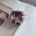 Dettaglio di uno scrunchie in velluto rosa con bordo in pizzo su un libro d'arte - Rosa