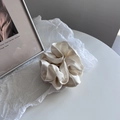Detail view of cream off-white satin scrunchie showing glossy fabric texture and soft pleats - Off White