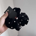 Detalle de un coletero de terciopelo negro con elegantes perlas blancas y etiqueta de marca - Negro