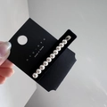 Dettaglio di 11 perle bianche lucide su una clip in metallo argento su carta di marca - Stile Perle Piccole