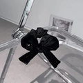Detail of a black velvet scrunchie bow hanging on a minimalist clear acrylic rack - Black