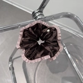 Détail d'un chouchou en velours marron avec bordure rose à volants et badge métal - Marron