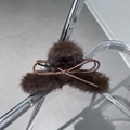 Detalle de una pinza de pelo de peluche marrón con lazo de cuero sobre fondo metálico - Marrón