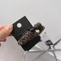 Detail einer braunen Tweed-Haarklammer mit Schleife und Goldanhänger auf Karte - BB-Clips / Geometrisches Braun