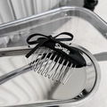 Detail eines schwarzen Leder-Schleifen-Haarkamms mit silberner Smile-Plakette auf Metall - Schwarz