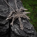 Macro detail of vintage gothic wing cross pendant on dark textured rock surface - Silver