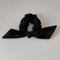 Detail view of a black satin scrunchie featuring a large bow and glossy silk texture - Black