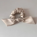 Detail of champagne satin bow scrunchie with silky ribbon and elegant ruched texture - Apricot