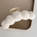 Detail of soft white faux fur claw clip with plush pom-poms on a display tray - White
