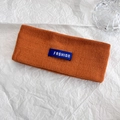Dettaglio della fascia invernale in maglia arancione con etichetta fashion su carta bianca - Arancione