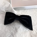 Detailed close-up of a premium black velvet bow hair clip on a textured background - Slanting Bow