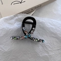 Dettaglio della molletta nera per capelli con strass colorati su sfondo di tessuto bianco - Nero