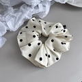 Detailed close-up of a cream satin polka dot scrunchie with a woven logo tag - Beige Polka Dot