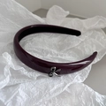 Dettaglio di un cerchietto bordeaux lucido con fiocco in metallo argento su sfondo strutturato - Fiocco Rosso Scuro