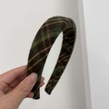 Gros plan d'un serre-tête rétro à carreaux en tissu vert foncé et coutures dorées - Vert