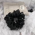 Close-up of black mesh scrunchie with white pearl accents on textured paper - Black