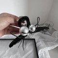 Macro detail of high-end black bow hair claw with silver foil spheres and logo tag - Black