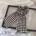 Vue détaillée d'un chouchou à carreaux noir et blanc avec rubans posé sur un plateau en verre - Style De Ruban