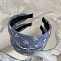 Dettaglio di un cerchietto in denim blu con ricami floreali bianchi su superficie a specchio - Stile a Bordo Largo