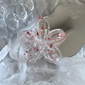 Detailed view of translucent plumeria flower hair claw with artistic colorful paint splatters - Pink + White