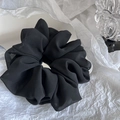 Detail of a large black silk-like hair scrunchie with soft ruffled textures on reflective surface - Black