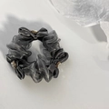 Detail eines grauen Organza-Haargummis mit einer zarten Schleife und funkelnden Strasssteinen - Grau