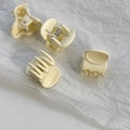 Detailed view of four mini cream-colored hair claw clips set on white textured paper - Beige