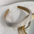 Dettaglio di un cerchietto in raso champagne con design bombato su carta testurizzata - Cammello Chiaro